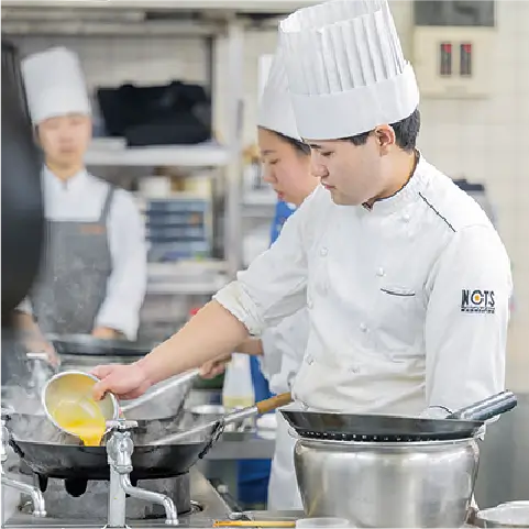 溶き卵を中華鍋に流し込む生徒